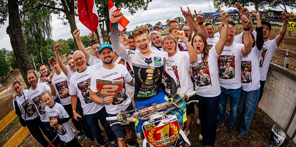 Skovbjerg Teambild Skovbjerg sitzt freudig auf seinem Motorrad, und um ihn herum steht sein Team.
