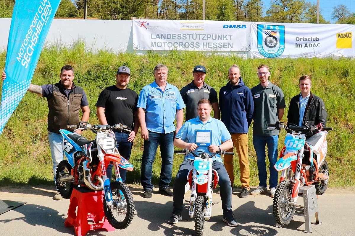 Gruppe von Personen vor dem Banner „Landesstützpunkt Motocross Hessen“ beim MSC Sechshelden, mit drei Motocross-Motorrädern im Vordergrund.