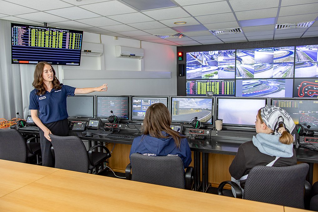 Discover Motorsport – Young Women's Edition 2026 in Oschersleben Eine Referentin erklärt im Race-Control-Raum die Monitorwände und die Abläufe der Rennleitung, während Teilnehmerinnen zuhören.