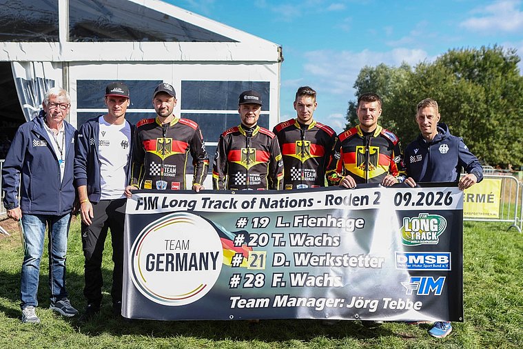 Von links: Josef Hukelmann, ehemaliger Teammanager, Michael Härtel, ehemaliger Fahrer und Teil der deutschen Nationalmannschaft, Dominik Werkstetter, Kapitän Lukas Fienhage, Timo Wachs, Fabian Wachs und Teammanager Jörg Tebbe Gruppenfoto der aufgereihten Deutschen Langbahn-Nationalmannschaft hinter einem Banner bei der Langbahn-Team-WM 2026 in Roden.