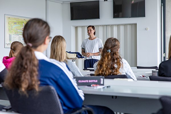 Discover Motorsport – Young Women's Edition 2026 in Oschersleben Lina van de Mars erklärt den Teilnehmerinnen im Pressecenter die Inhalte des Aktionstags, während die Schülerinnen aufmerksam zuhören.