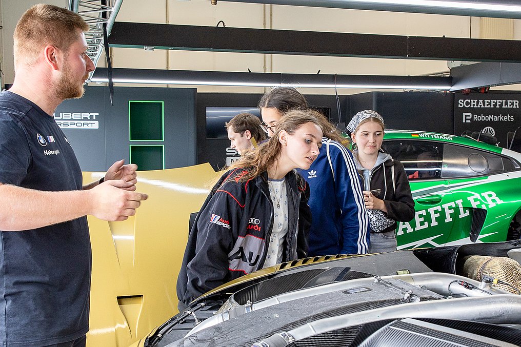 Discover Motorsport – Young Women's Edition 2026 in Oschersleben Ein Mechaniker erklärt einer Gruppe von Teilnehmerinnen die Technik eines DTM-Autos in der Schubert-Motorsport-Garage.