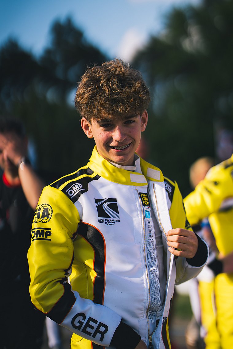 Stavros Tsotsos Francia im Rennanzug, kurz vor seinem Einsatz in der FIA Karting Academy Trophy, mit einem Lächeln in Richtung Kamera.