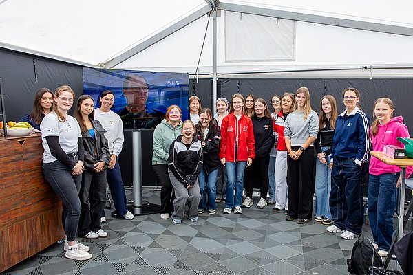 Discover Motorsport – Young Women's Edition 2026 in Oschersleben Die Teilnehmerinnen haben sich in einem Zelt vor dem Fernseher positioniert, der eine Videobotschaft von Ellen Lohr von AVL-RACETECH zeigt
