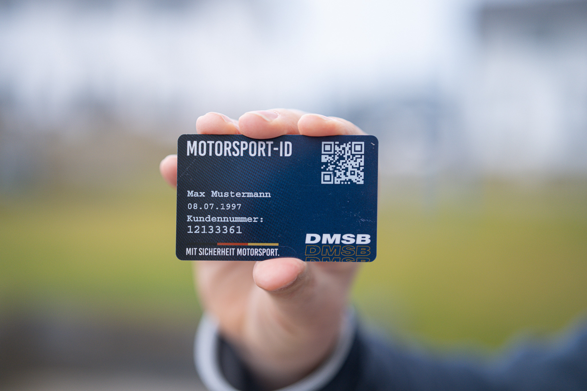 Eine Hand hält eine Motorsport-ID-Karte mit Text und einem QR-Code, der deutlich im Mittelpunkt steht.