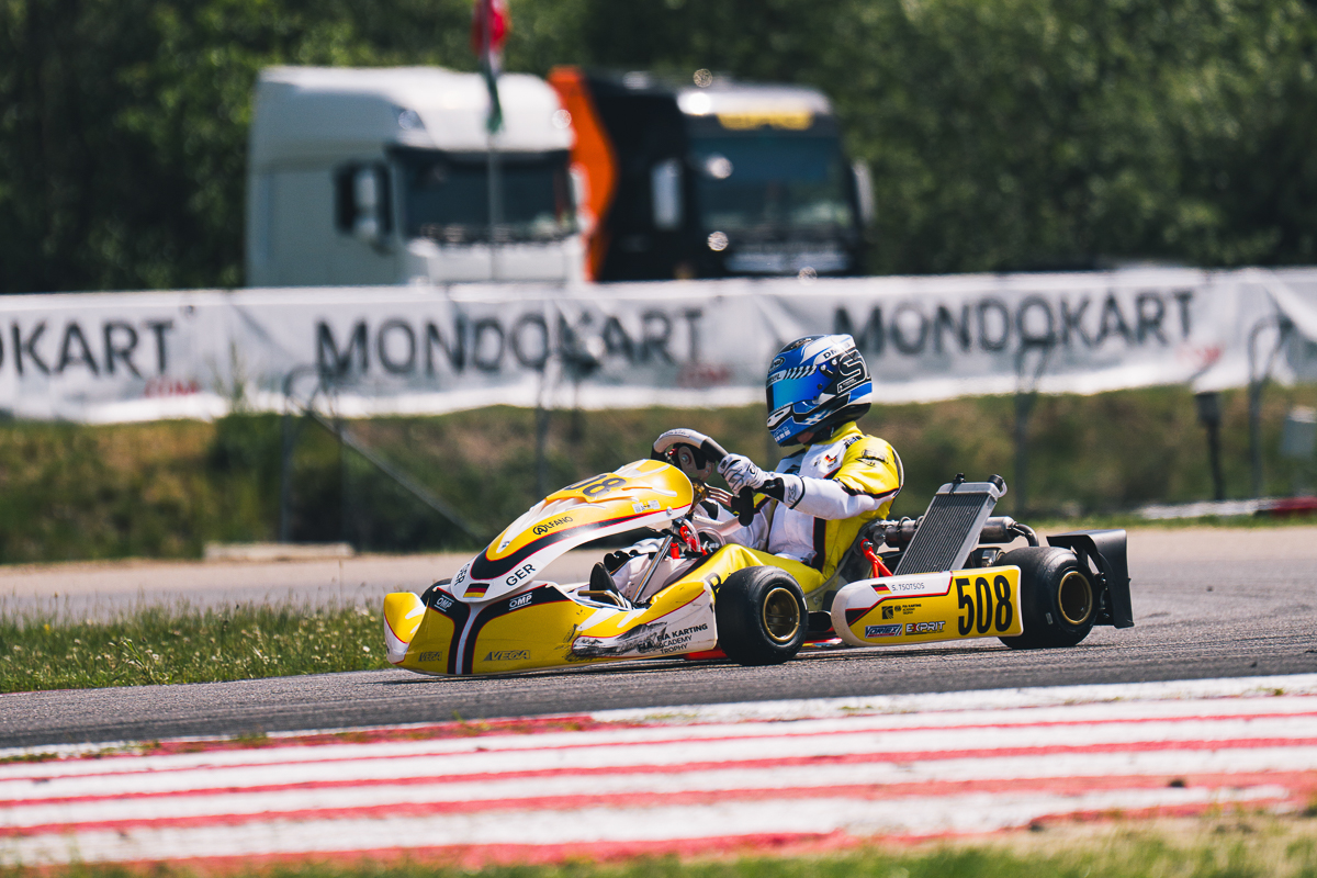 Stavros Tsotsos Francia, FIA Karting Academy Trophy Junior, Genk 2026 Stavros Tsotsos Francia fährt im gelben Kart durch eine Kurve der FIA Karting Academy Trophy, im Hintergrund sind MONDOKART-Banner und Transportfahrzeuge zu sehen.